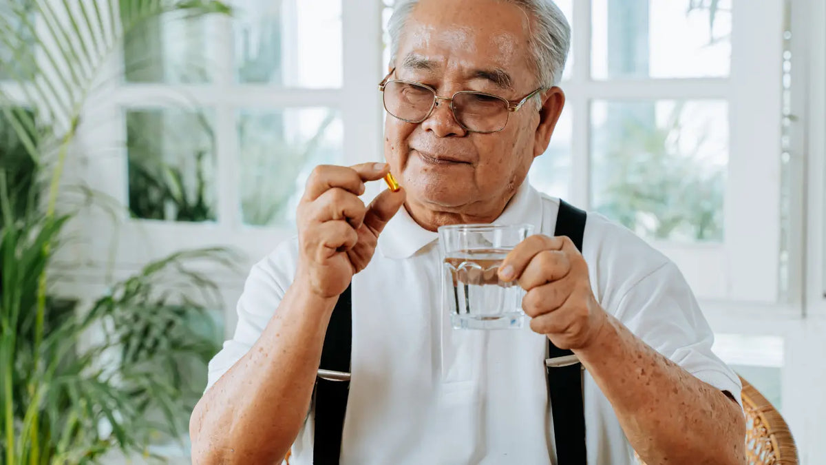 Älterer Mann hält Wasserglas uns Supplement in den Händen.