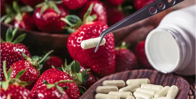 Pinzette mit Kapsel des Nahrungsergänzungsmittel vor Erdbeeren im Hintergrund 